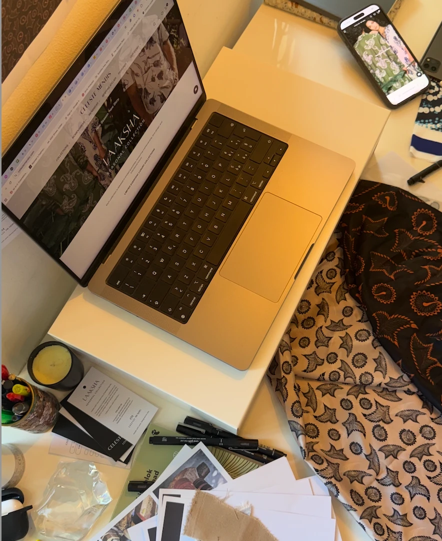 Studio desk with the LAAKSHA collection on the laptop, print fabrics, swing tags and sketch pens