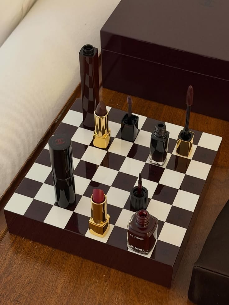 Lipsticks and nail lacquers arranged like pieces on a burgundy and ivory chessboard
